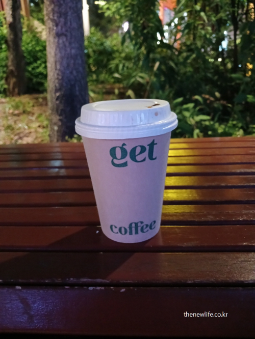 밤에 공원 벤치 위에 놓인 테이크아웃 커피 컵