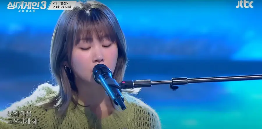 싱어게인 3- 파란색을 배경으로 연두색 상의를 입고 단발머리를 늘어뜨린채 두눈감고 노래하는 60호 상반신