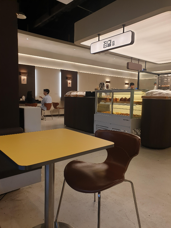 간접조명이 있는 정밀 중앙 베이커리와 주변 노랑 테이블로 구성되어 있다.