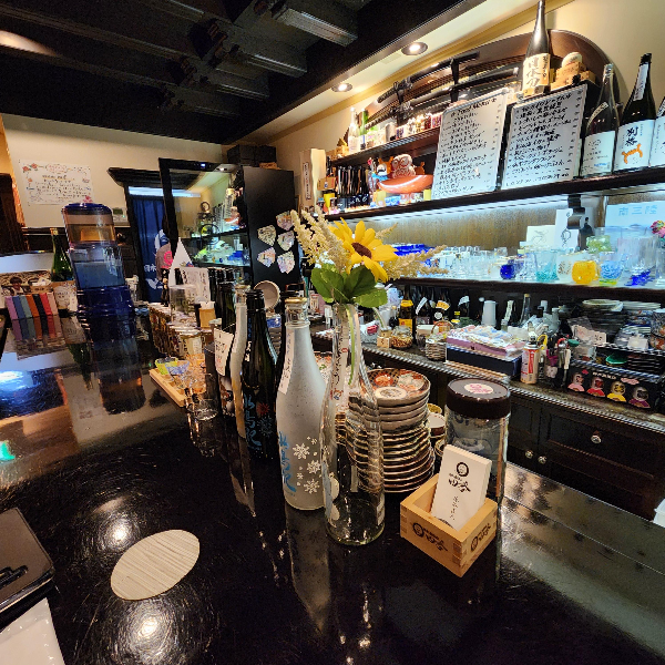 테이블 위에 빈 사케병 4 개가 놓여 있고 뒤쪽에는 다양한 컵 들이 보인다.