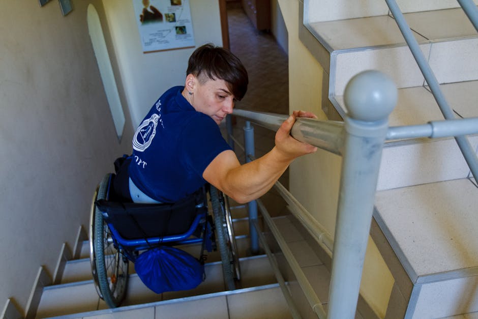 A determined individual in a wheelchair on stairs, using a handrail for support.