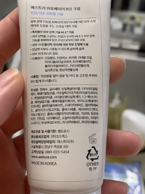 피부과 레이저 시술 후 안전한 보습을 위해 에스트라 아토베리어365 크림 뒷면의 전성분표와 인공향료 등 10무첨가 표시를 꼼꼼하게 확인하는 모습