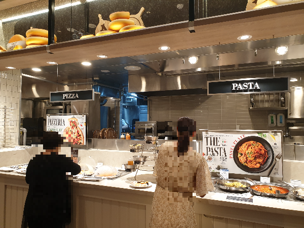 피자 및 파스타 코너 두 명의 고객이 음식을 담고 있다.