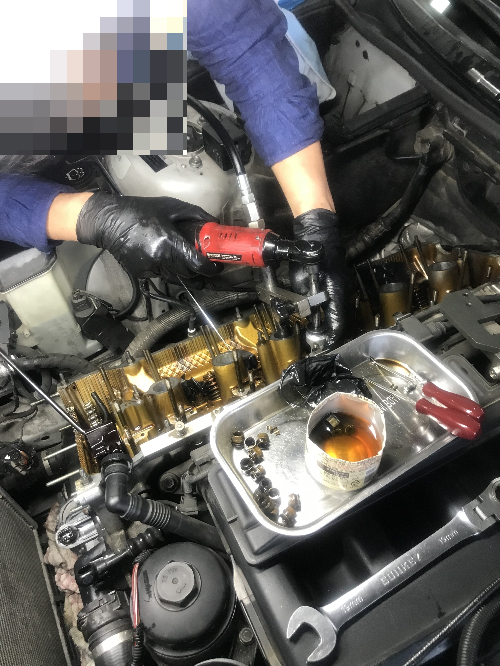 정비사가 BMW 엔진의 밸브 스템씰 교체를 위해 전동 공구로 분해 작업을 진행 중인 모습