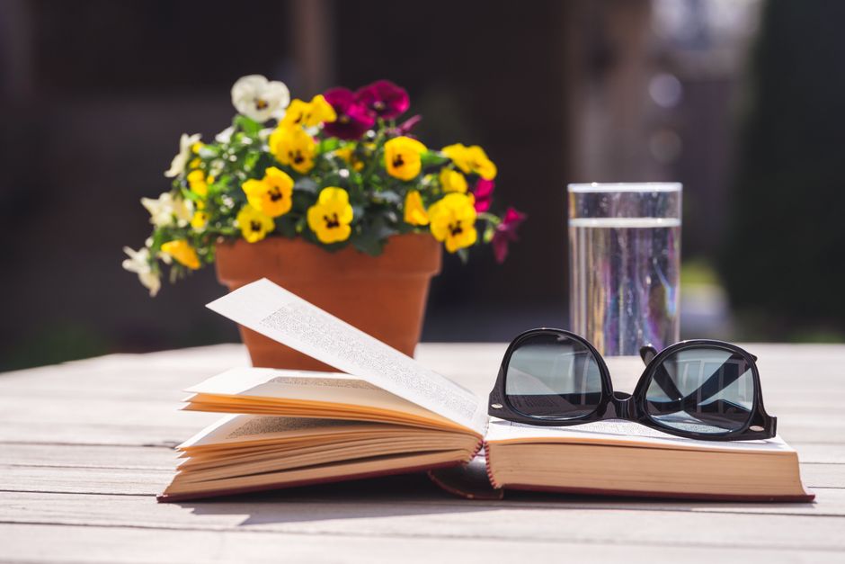 A peaceful outdoor scene featuring a book, sunglasses, and a pot of pansies.