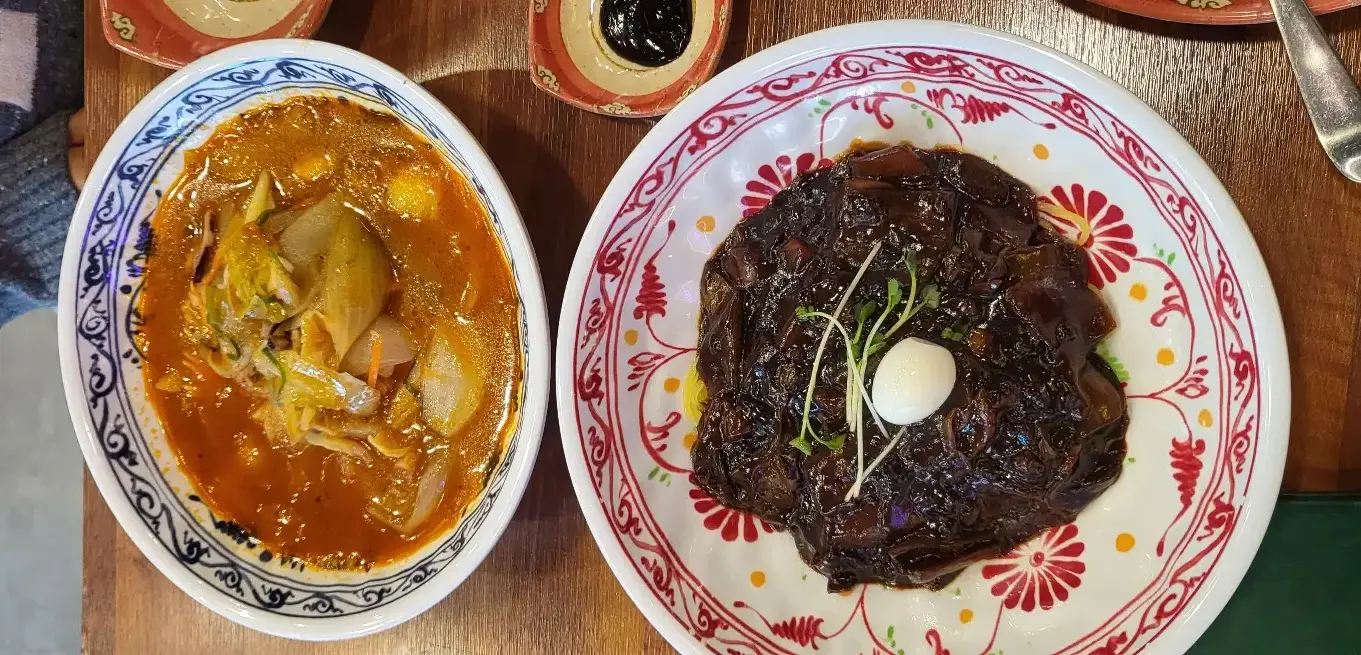 보배반점 -
나무 테이블위 흰색 바탕 파란 줄무늬 야채와 해산물이 가득 들어있는 주황색 짬뽕과 흰색바탕 빨간줄무늬 그릇안 담긴 까만 자장면 위 흰 메추리알과 새싹채소