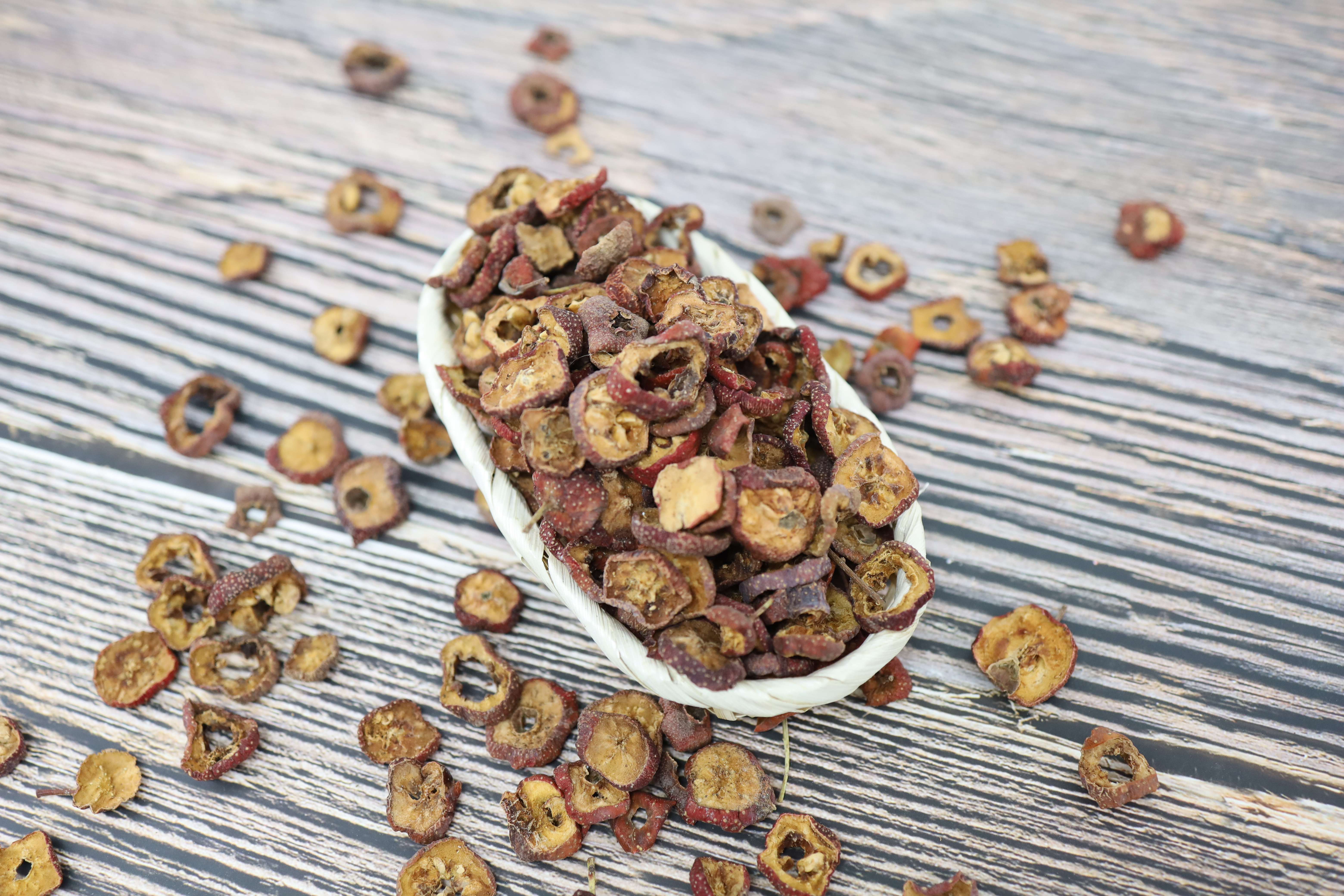 야생의 산사나무에서 채취를 한 산사나무 열매인 아가위(산사)를 깨끗이 세척을 한 후에 편으로 잘라서 바싹 말린 것을 마룻바닥 위에 흰색 그릇을 놓고 가득 담아 놓고, 그 주변에 산사를 많이 흩어 놓은 사진