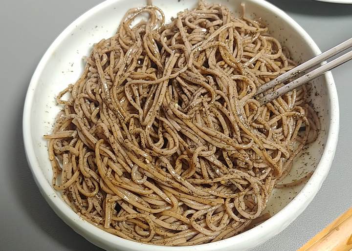 사기그릇에-검은색-김가루가-뭍혀진-갈색-메밀면이-있고-은색-젓가락이-면의-오른쪽에-꼽혀있다