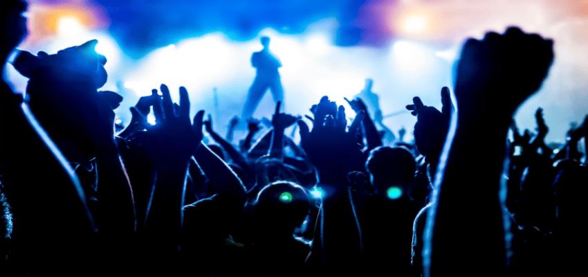 밝은 조명 아래 열광하는 관객들이 손을 들고 공연을 즐기는 모습