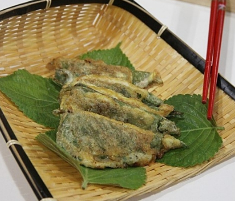 깻잎을 반으로 접어 속에 고기 다진 것을 넣고 튀김옷을 입혀서 튀긴 갯잎튀김을 대나무로 만든 갈판에 깻잎을 깔고 그 위에 4개를 빨간색 젓가락과 함께 놓아두고 찍은 사진