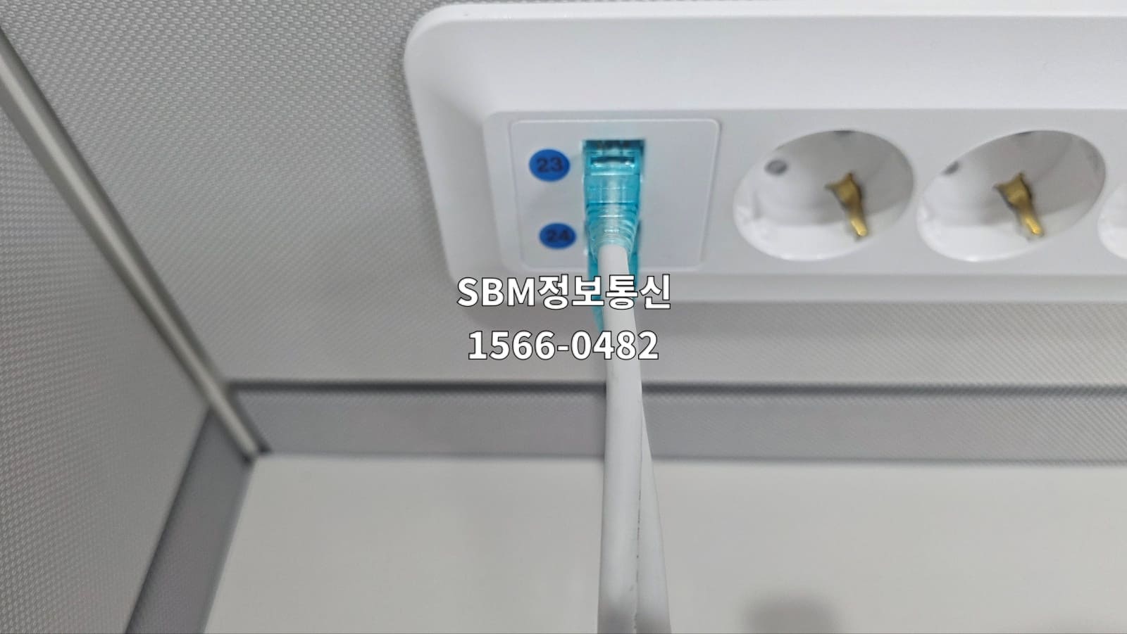 사무실 파티션 하부의 빌트인 네트워크 포트에 흰색 랜선을 꽂아 데스크톱 연결을 준비한 모습.