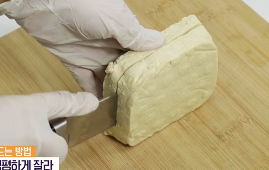 네모난-두부를-도마에-올리고-장갑을-낀-손으로-칼을-이용해-두부를-자르는-모습