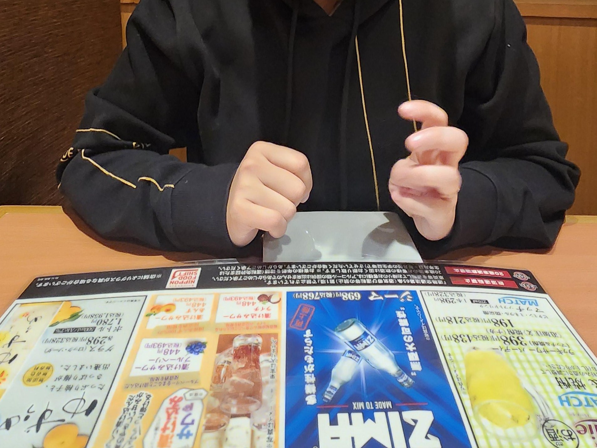 테이블 위에 메뉴가 있고 그 메뉴판을 보고 있는 사람의 손이 보인다.