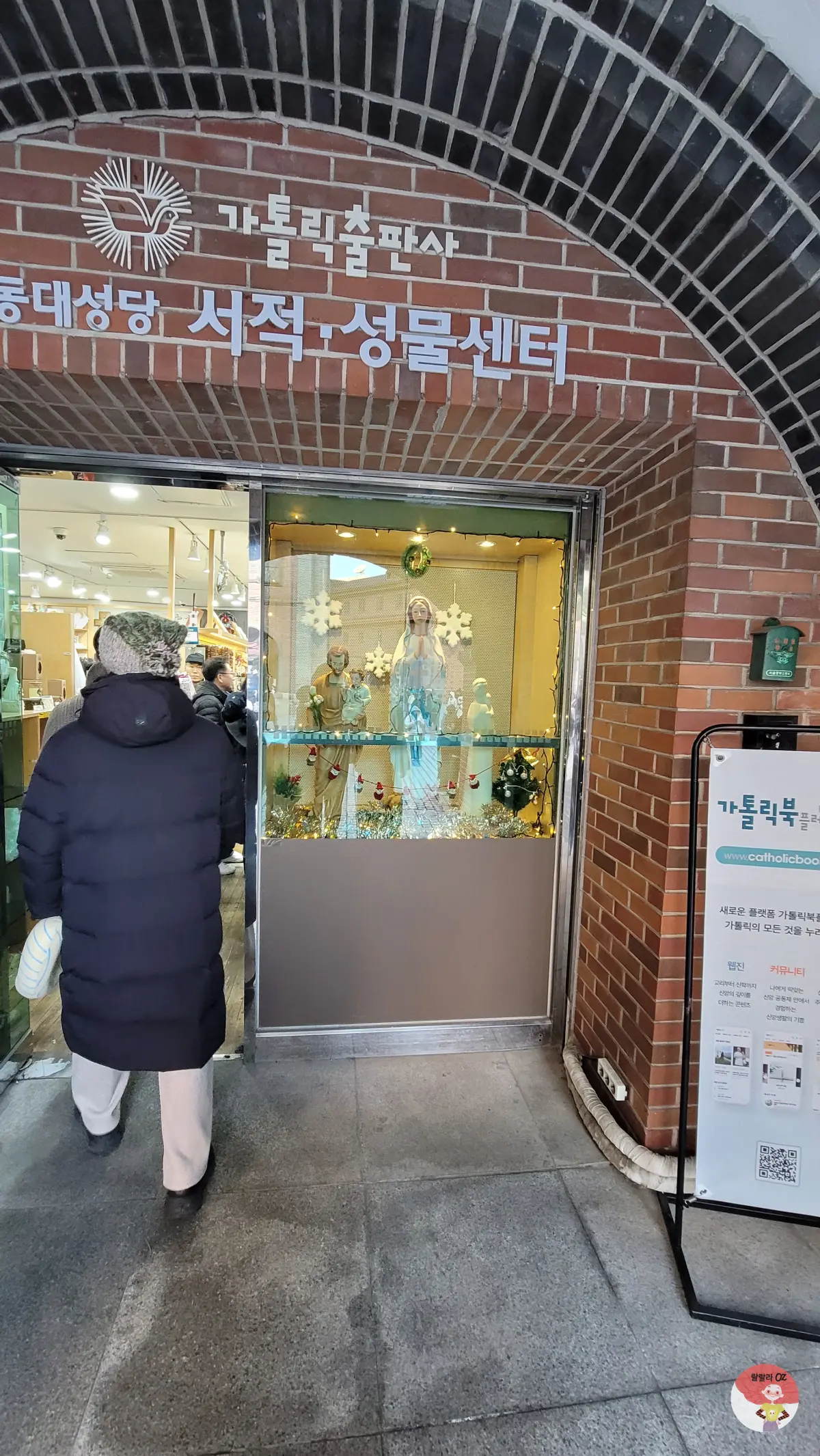 명동성당, 가톨릭출판사 외관, 진열장에는 성모 마리아상과 크리스마스 장식이 보이며, 입구 옆에는 안내판이 있다.