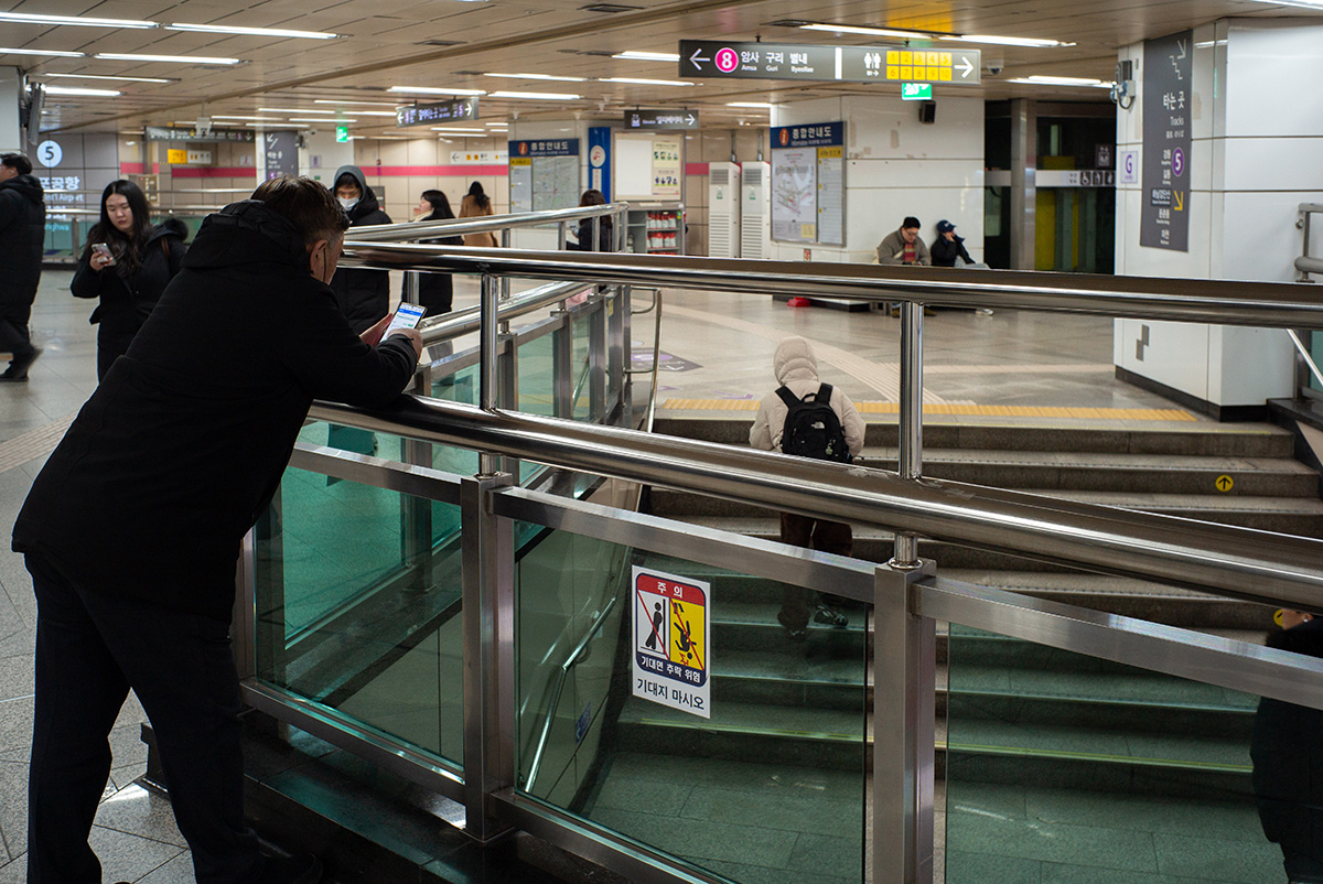 지하철 역사에서 에스컬레이터를 내려다보는 인물과 대기 공간, 라이카 M-P Typ 240의 자연스러운 실내 색감으로 담은 거리 사진