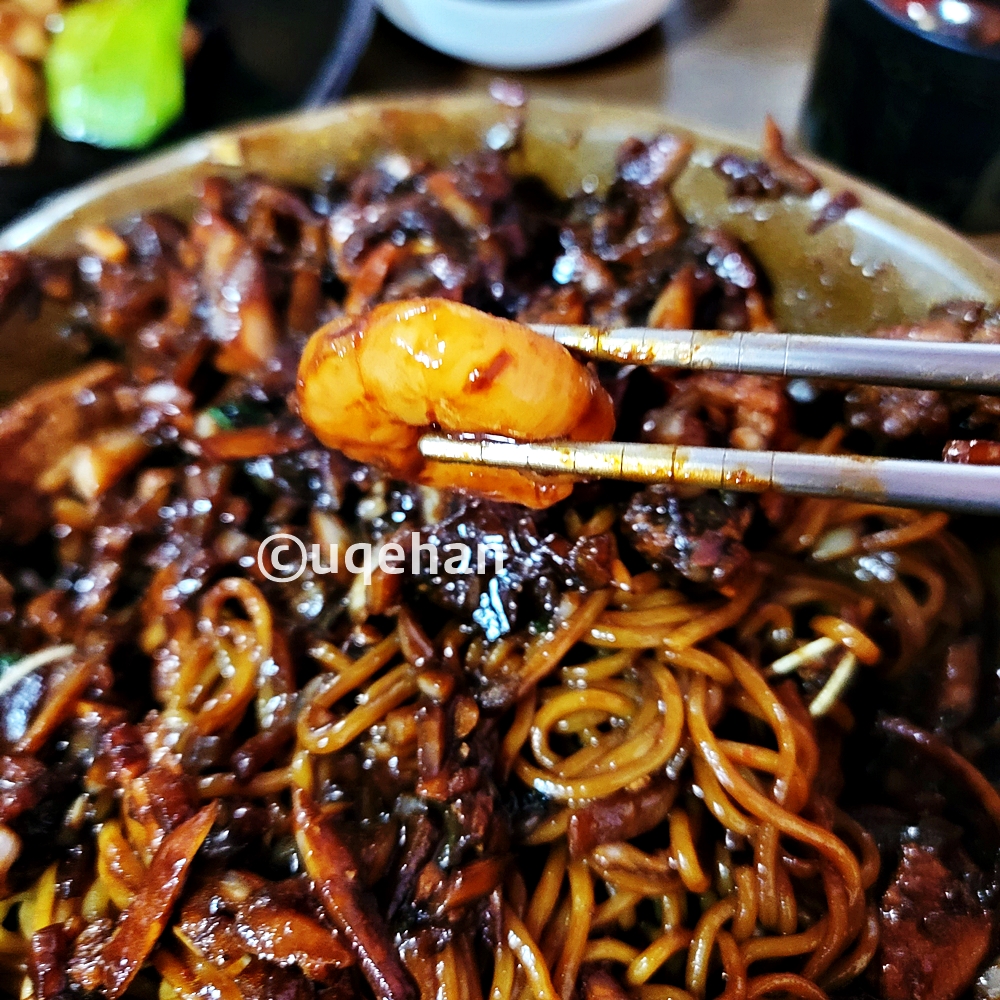 아랫쪽에는 짜장면이 있고&amp;#44; 간짜장 안에 들어있는 새우를 젓가락으로 들고 있는 사진이다.