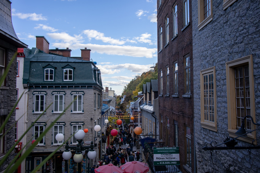 푸른빛 지붕과 회색 벽돌이 있는 창문이 있는 집이 왼쪽에 있고, 골목 사이로 전등이 연결되어 있다. 오른쪽으로는 건물이 연결되어 있다.