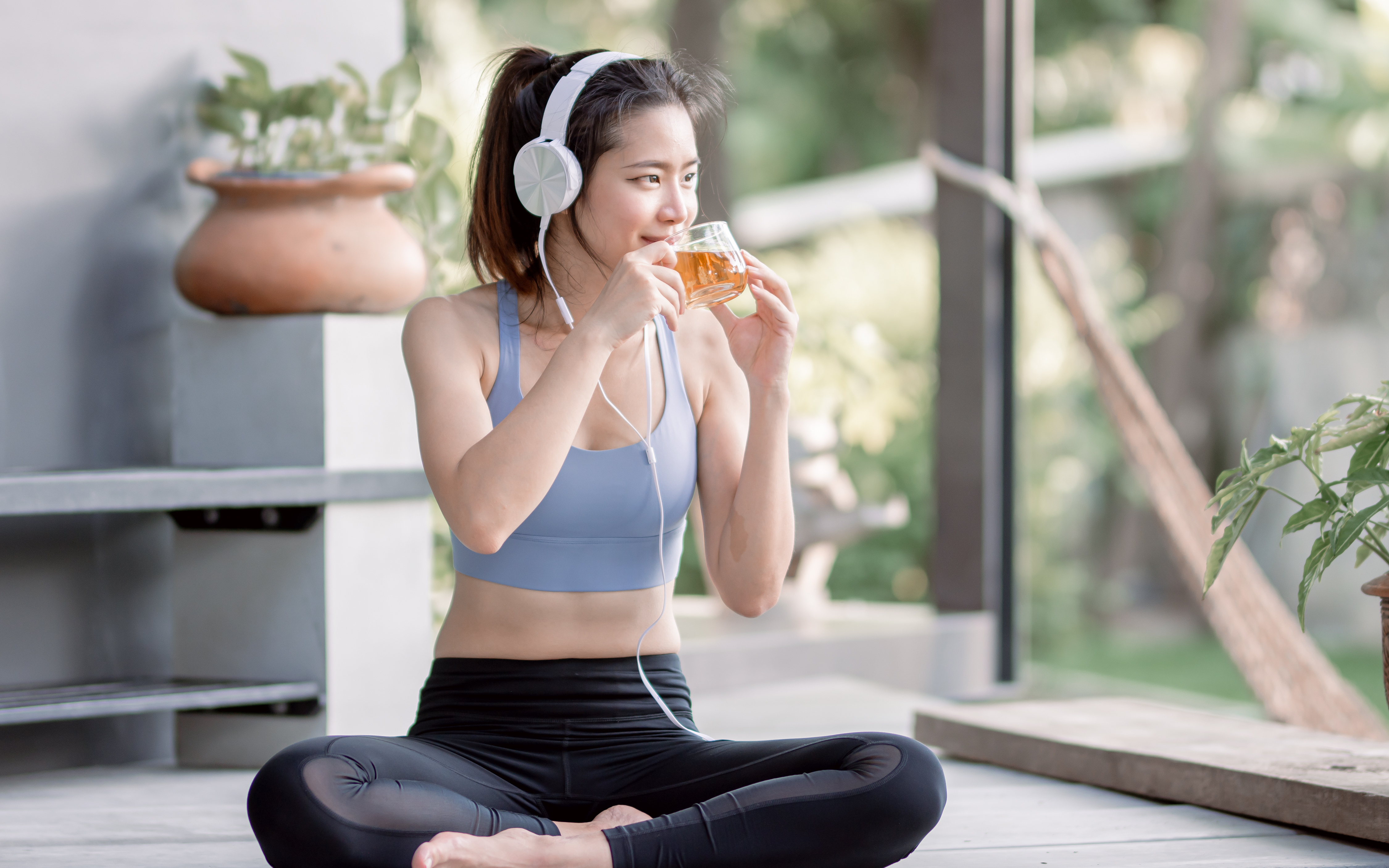 운동을 마친 여성이 헤드셋을 착용한 채로 허브티를 마시며 여름철 다이어트 루틴을 실천하는 모습
