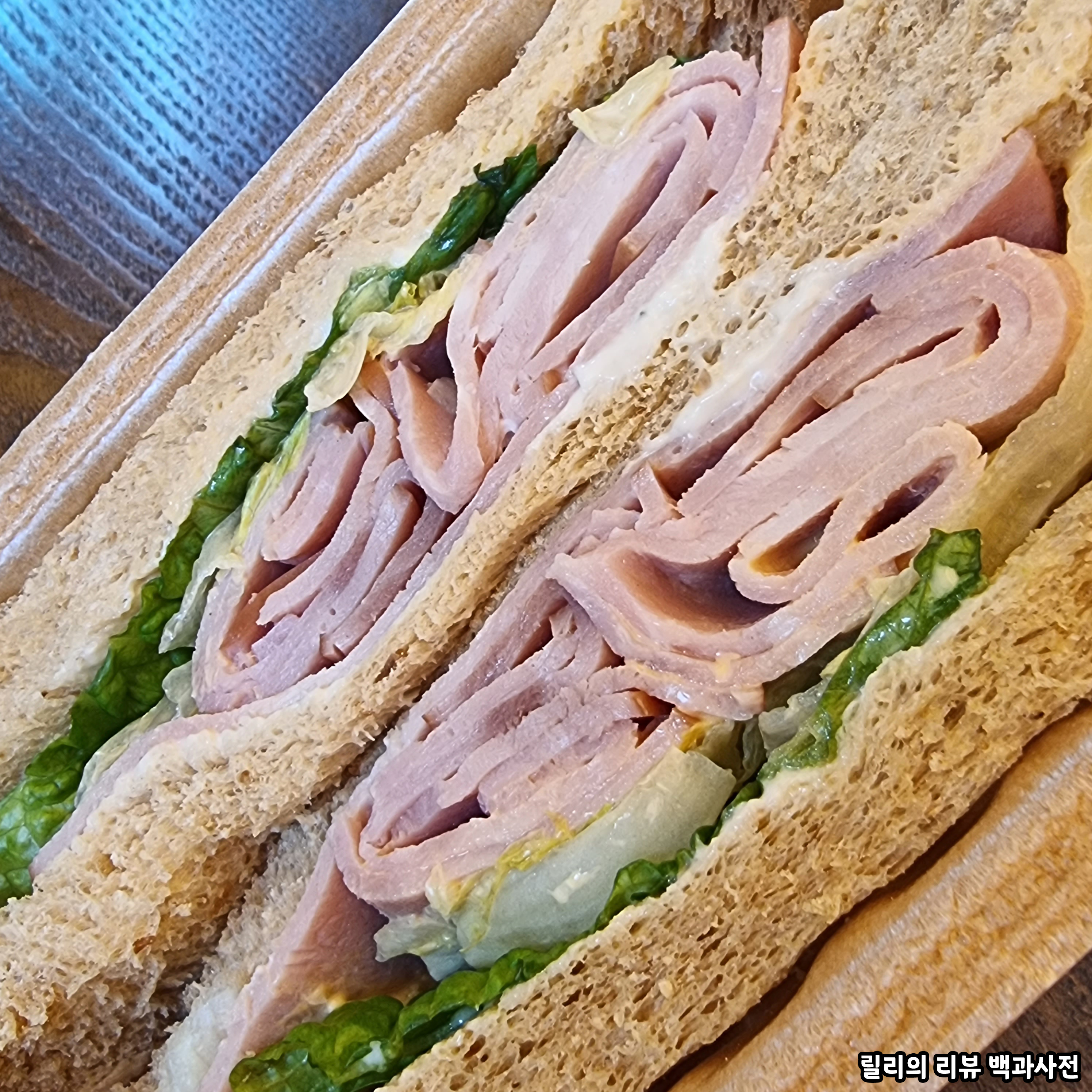 샌드위치 단면 사진. 빵 사이에 치즈 두 장&#44; 양상추&#44; 햄이 들어있음