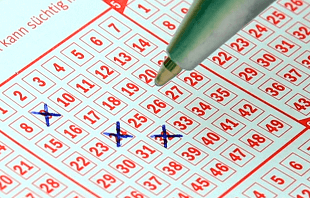 숫자가 가득 적힌 로또 용지가 있고 볼펜으로 숫자 3개에 X 표시를 하고 있다.
