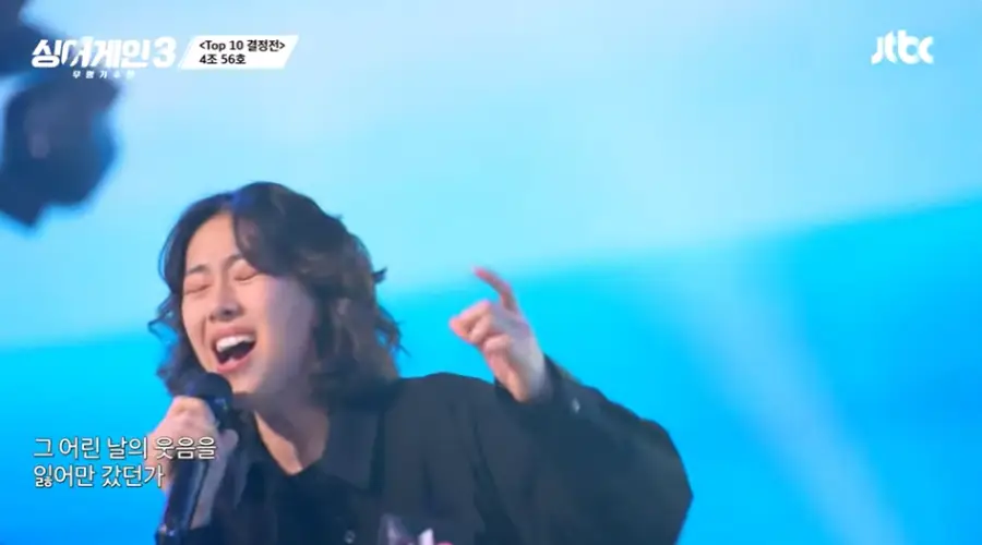 싱어게인3- 파란배경 검은옷을 입은 여자가 오른손을 들고 노래하는 모습