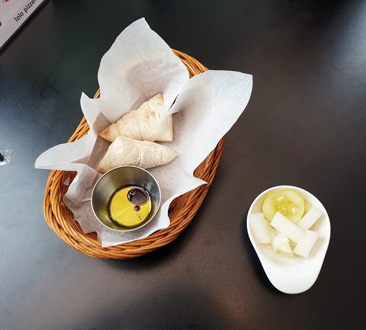 이올로화덕피자-두개의-식전빵과-올리브유가-함께-나무바구니에-들어있다-옆엔-피클이-있다