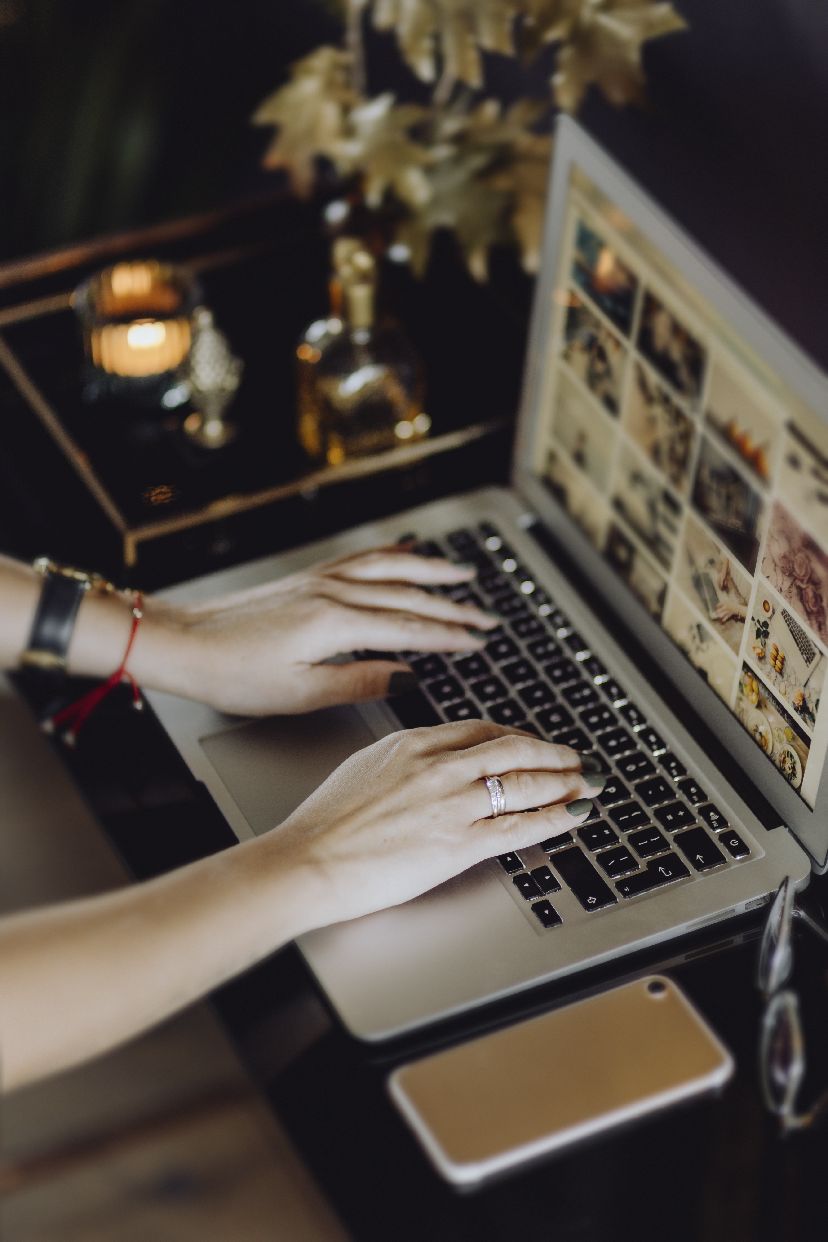 노트북 키보드를 타이핑하고 있는 손, 화면에는 블로그가 열려있고 테이블 위에 스마트폰과 따뜻한 조명이 있는 카페 작업 환경