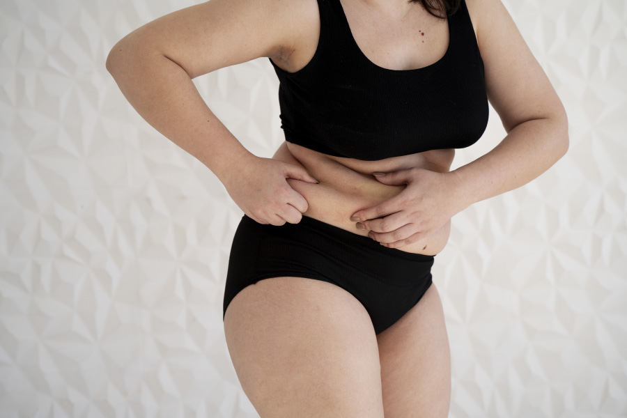 비만인 여성이 옆구리에 있는 살을 양쪽 손으로 쥐며, 옆구리 비만을 고민하고 있는 사진