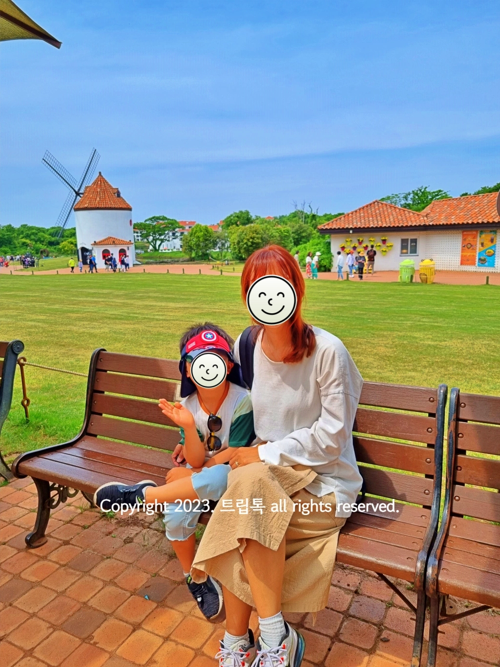 벤치에 앉은 두사람 뒤로 풍차와 잔디가 펼쳐져있다.