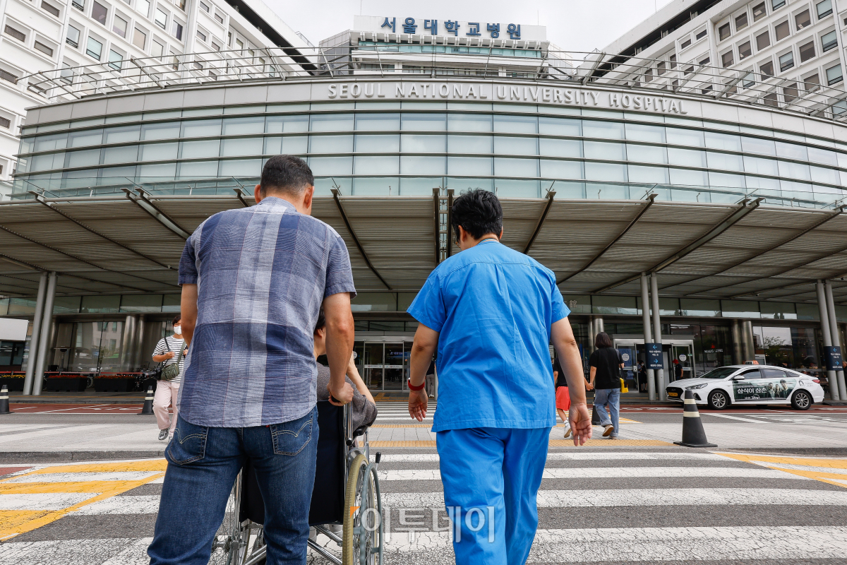 휠체어에 탄 환자를 이송중인 의사와 환자보호자