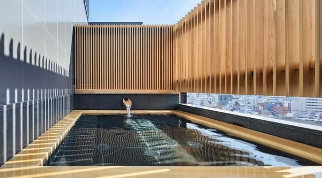 밖으로 빌딜이 보이고 나무로된 넓은 목욕탕에 물이 받아져 있다.