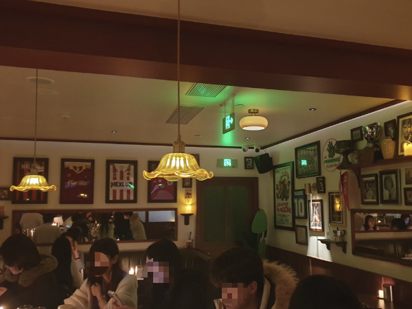 어두운 조명, 흰 벽과 천정, 그리고 나무 대들보, 벽면에는 각종 액자들이 배치되어 있다.