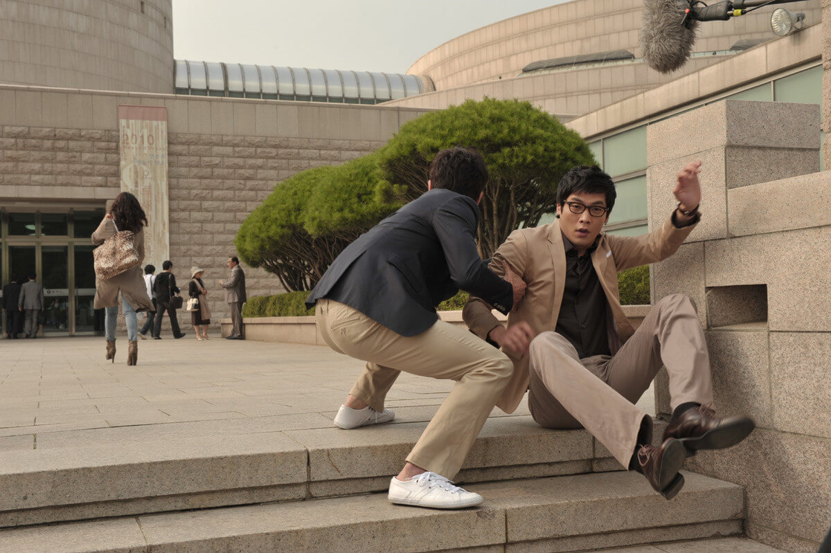 계단에서 넘어진 남자를 다른 남자가 부축하고 있는 모습
