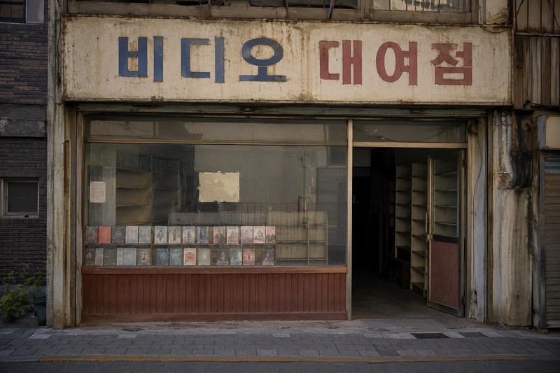 빛바랜 비디오 대여점 간판 아래 빈 선반과 일부 테이프만 남은 가게가 문을 닫은 모습