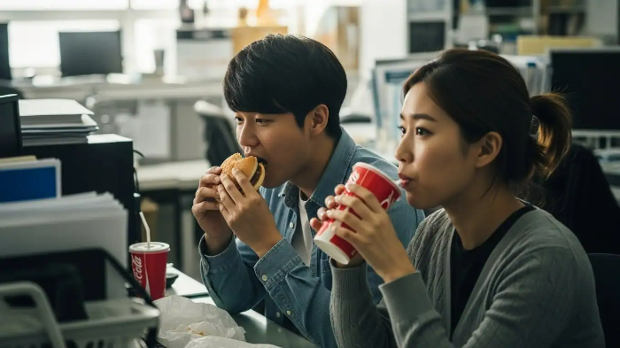 사무실에서 직장인 남자와 여자가 햄버거와 콜라로 점심을 먹고 있는 모습