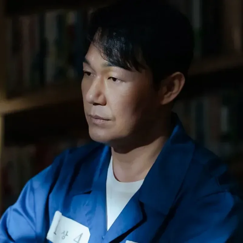 감방을 배경으로 파란 죄수복을 입고 앉아 있는 국민사형투표의 권석주