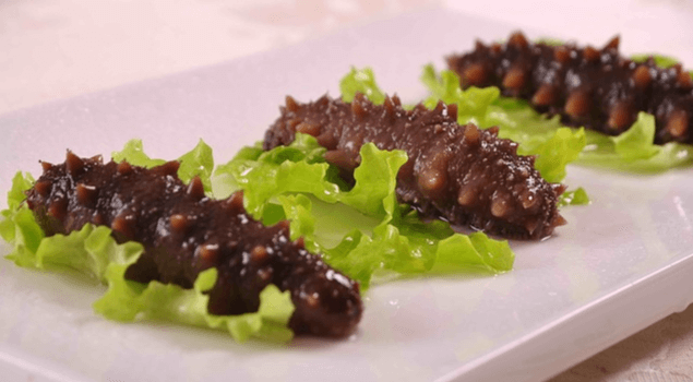 네모난 하얀 접시에 해삼 3마리가 가지런히 놓여있고 각 해삼 아래에는 연두색 상추가 한장씩 깔려있다.