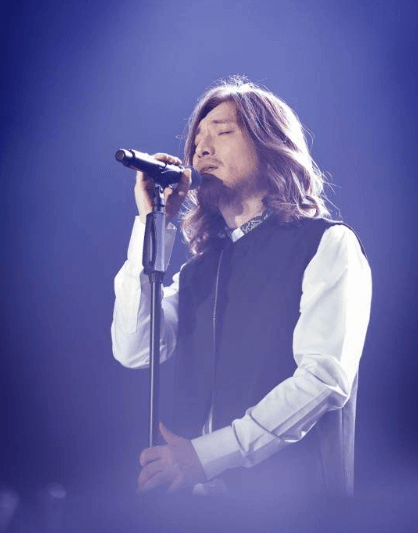 임재범이-하얀-셔츠와-조끼를-입고-스탠딩-마이크를-쥐고-노래를-부르는-모습