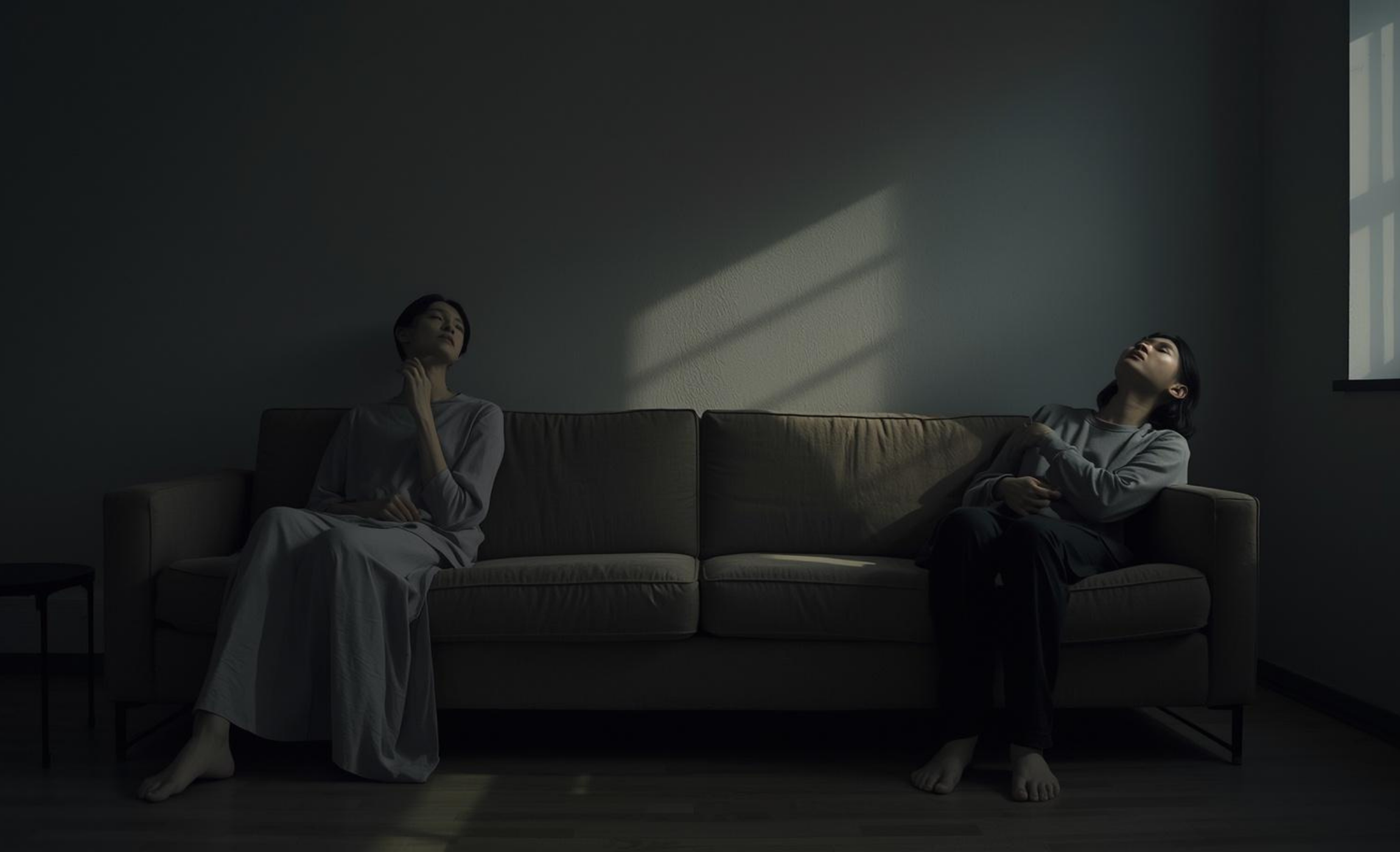 미니멀한 공간의 긴 소파 양끝에 앉아, 한 명은 대화하려 몸을 틀고 한 명은 조용히 창밖을 바라보는 두 중성적 인물의 외롭고 애틋한 모습
