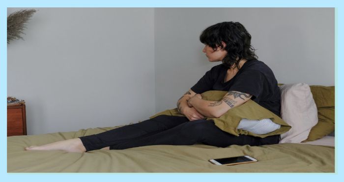 침대에 앉아 쿠션을 끌어안고 멍하니 바라보는 여성의 사진. 우울감이나 무기력감을 표현한 모습. 