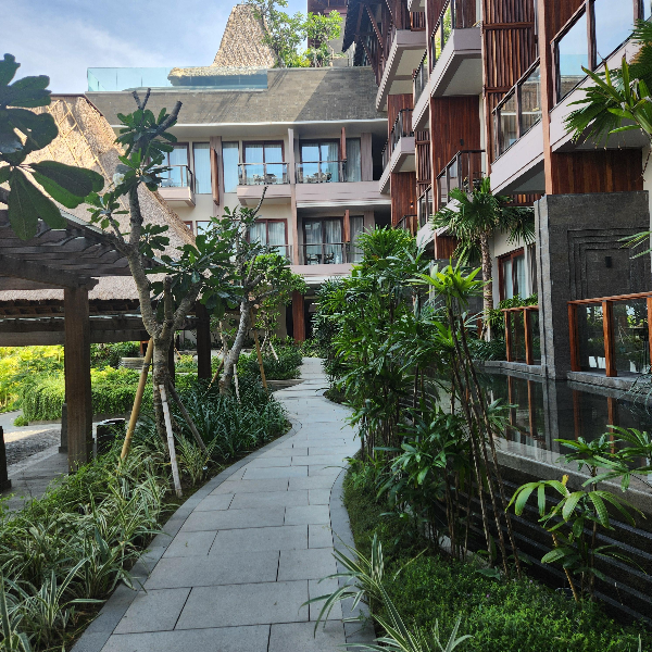 좁은 길 양 옆으로 나무와 풀이 있는 곳. 3층 높이의 호텔 건물