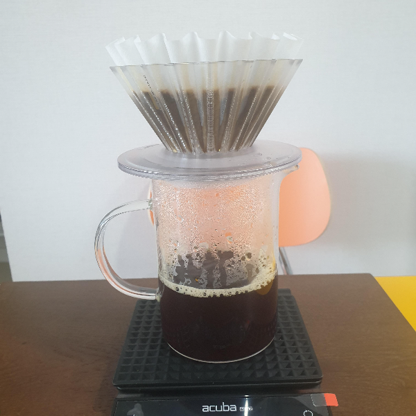 웨이브형 필터가 장착되어 있는 오리가미 드리퍼가 서버 위에 올라가 있다. 커피가 추출 되어 서버에는 커피가 담겨있다.