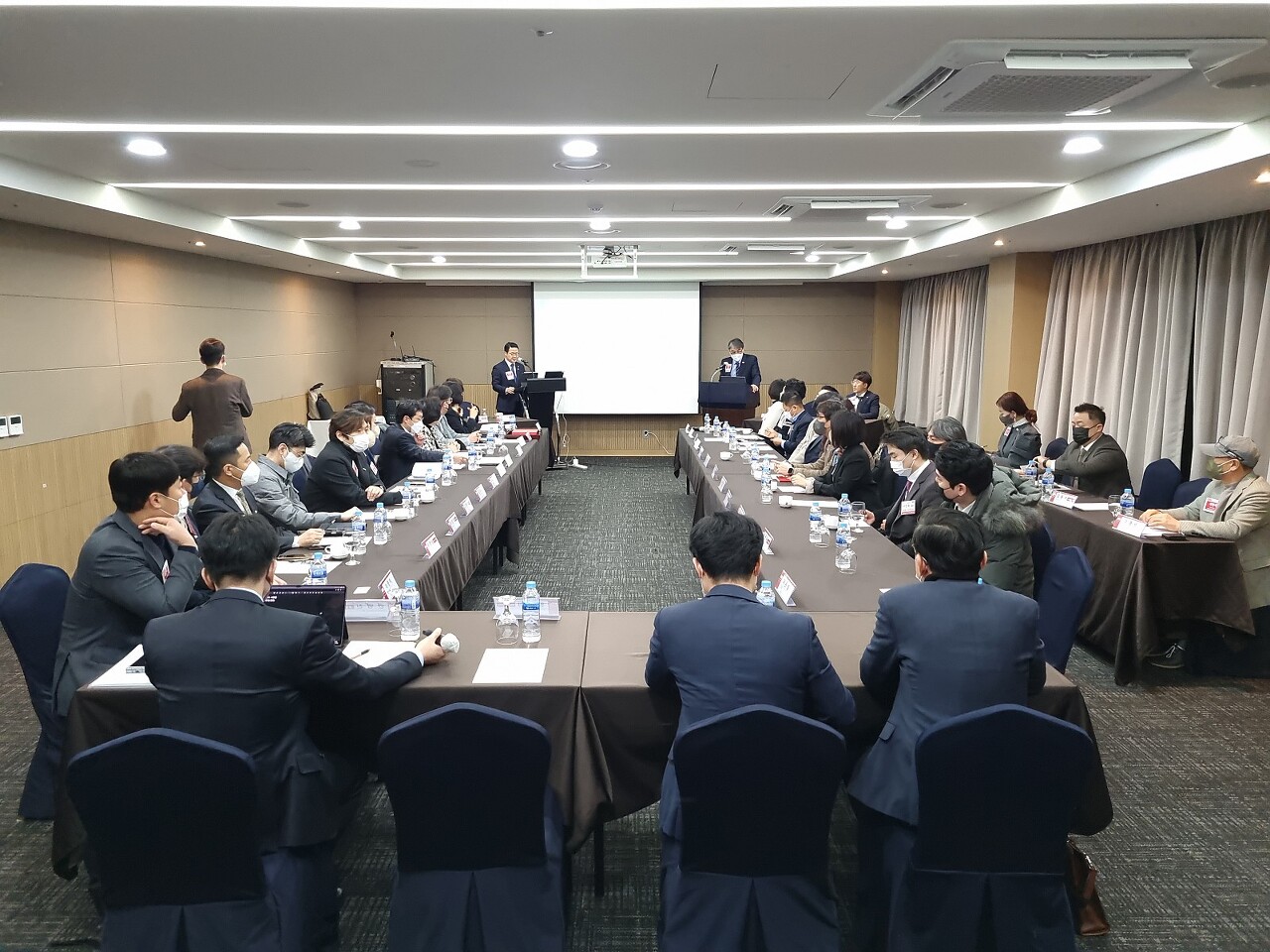 비엔아이 그랜드 챕터의 주간회의 장면입니다. ㄷ자형 회의실 테이블에서 30여명의 멤버들이 한기만 의장의 발표를 듣고 있습니다.