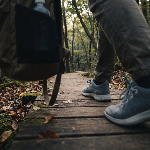 화담숲의 나무 데크 산책로를 걷고 있는 편안한 메리노울 운동화의 클로즈업 샷. 부드러운 햇살과 자연스러운 숲의 질감이 신발의 포근한 텍스처와 어우러진 시네마틱한 지면 높이의 라이프스타일 사진