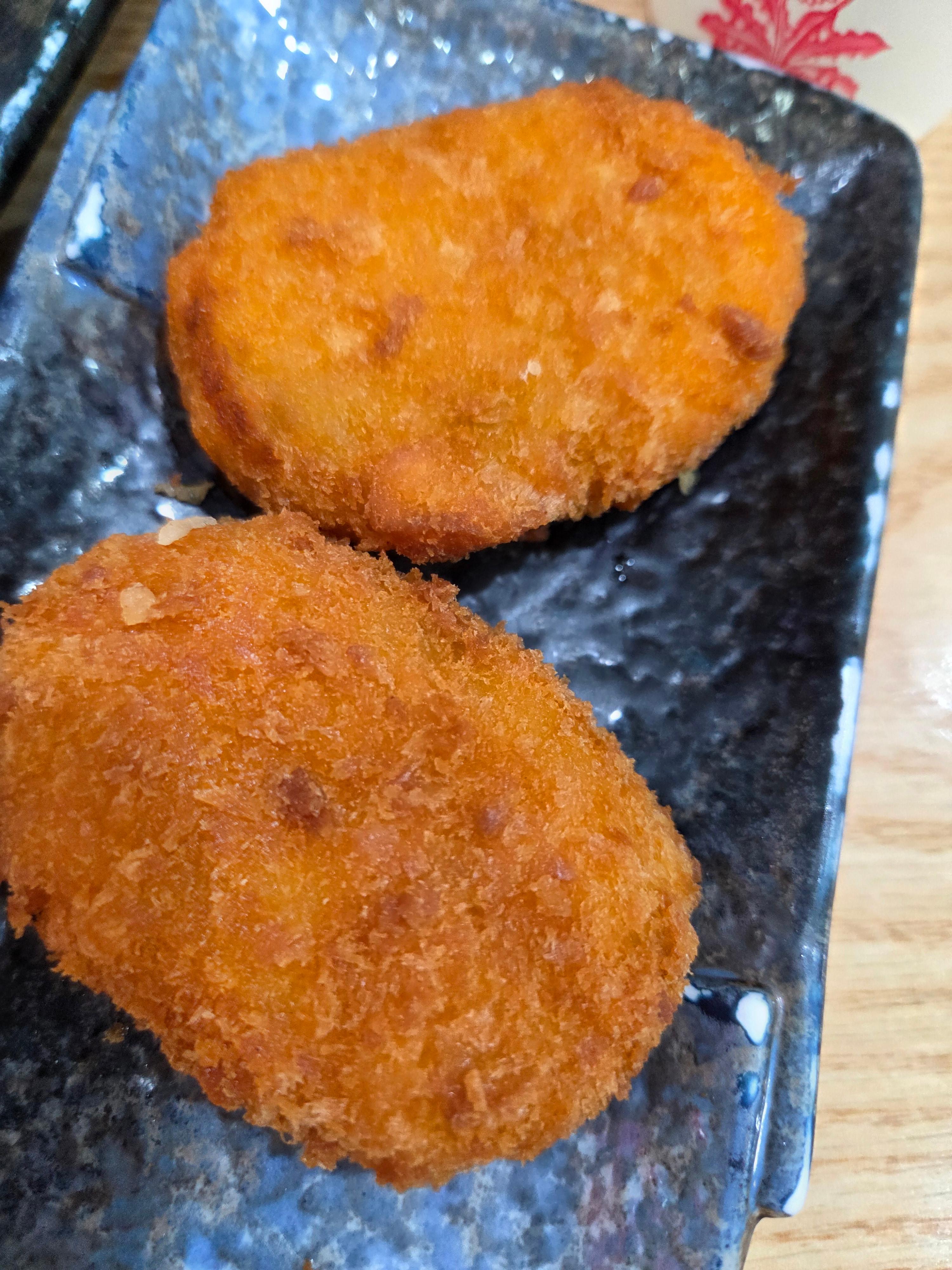 검은 접시에 담긴 노릇하게 튀겨진 고구마 감자 고로케 두 개 모습