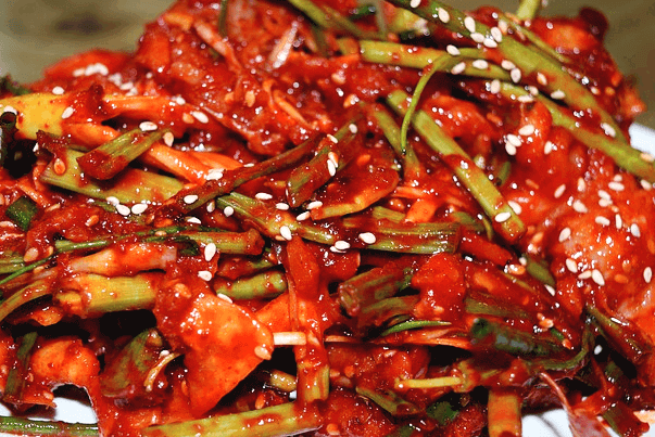 하얀 접시에 빨간 고추가루로 잘 버무려진 골뱅이무침이 가득 담겨 있다. 위에는 초록색의 부추가 얹어있고 깨소금도 뿌려졌다.