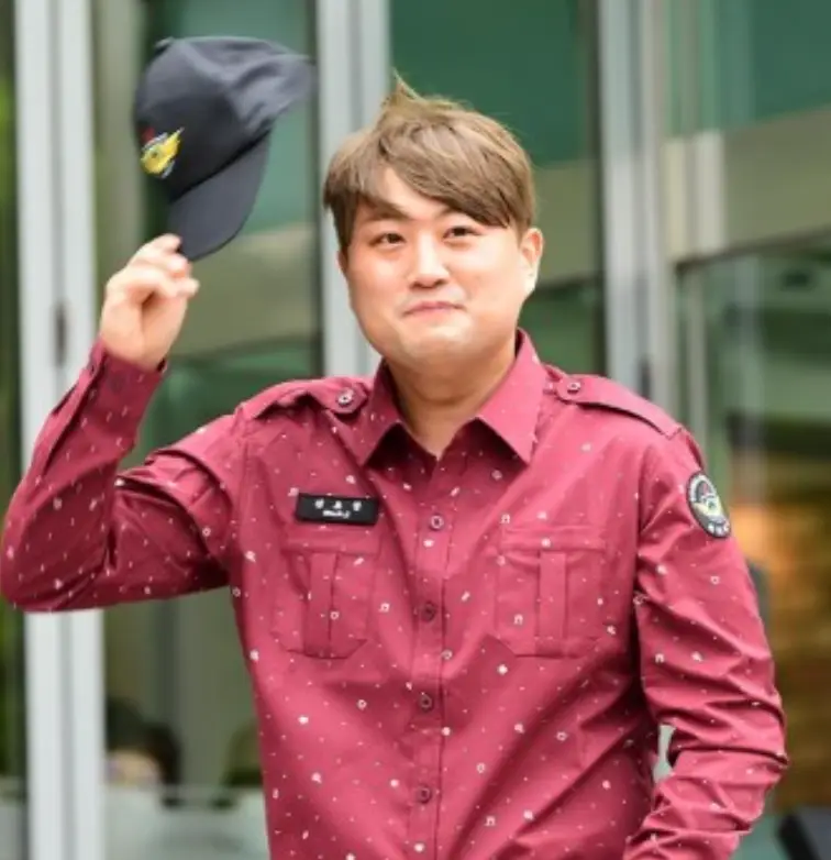 밝은 외부 빨간 셔츠 모자를 오른손으로 들어올린채 미소짓는 김호중