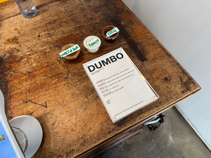 파리 마레 DUMBO 매장 내 로고가 적힌 메뉴판과 스위트앤사워, 랜치, BBQ 소스가 놓인 빈티지한 우드 테이블.