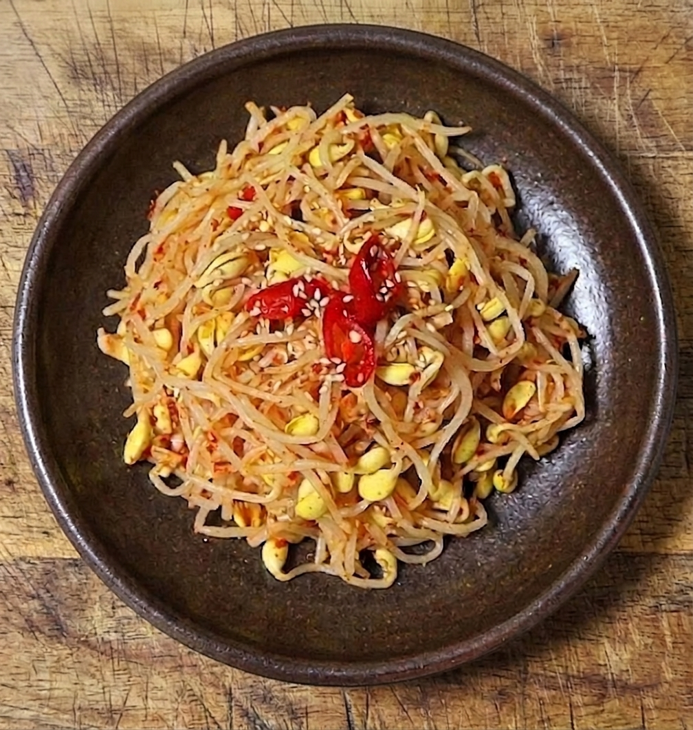 고춧가루와 홍고추 고명으로 맛을 낸 아삭한 빨간 콩나물무침 반찬 이미지.