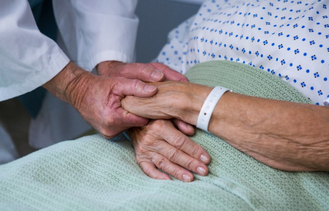 한 병상에 앉아있는 노인의 손을 잡아주는 의사